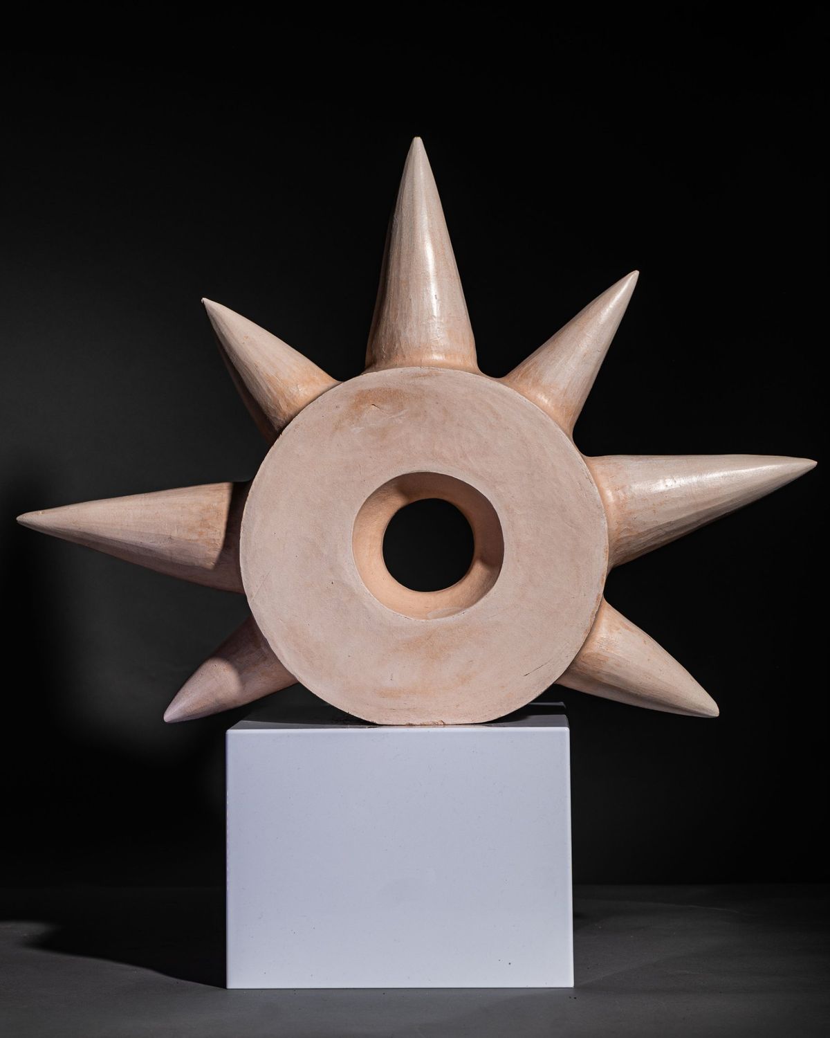 Pale terracotta star-form sculpture with a central opening, on a white plinth