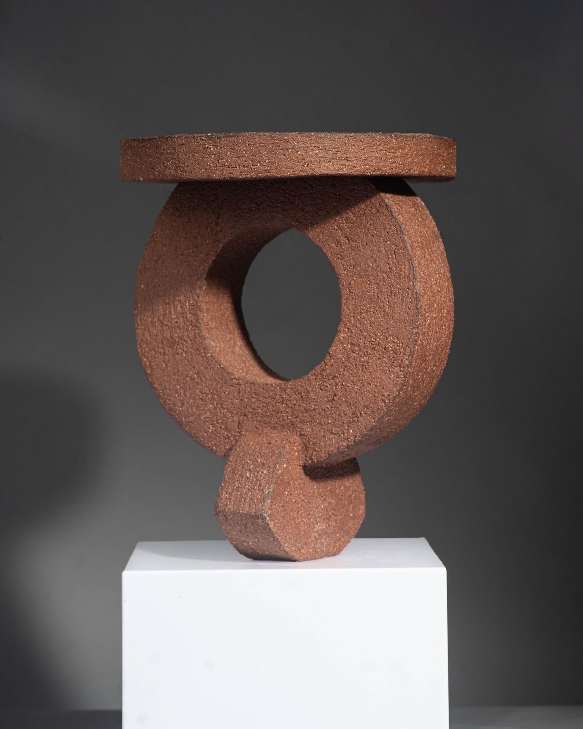 Textured terracotta ring sculpture balanced beneath a flat disc