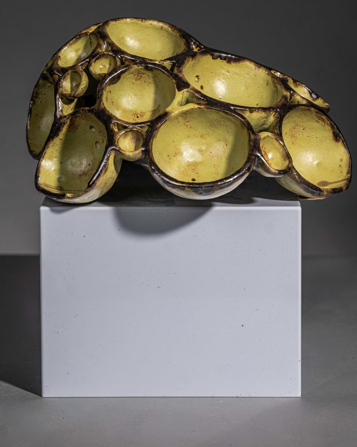 Low olive green glazed sculpture of clustered bowl forms on a white plinth