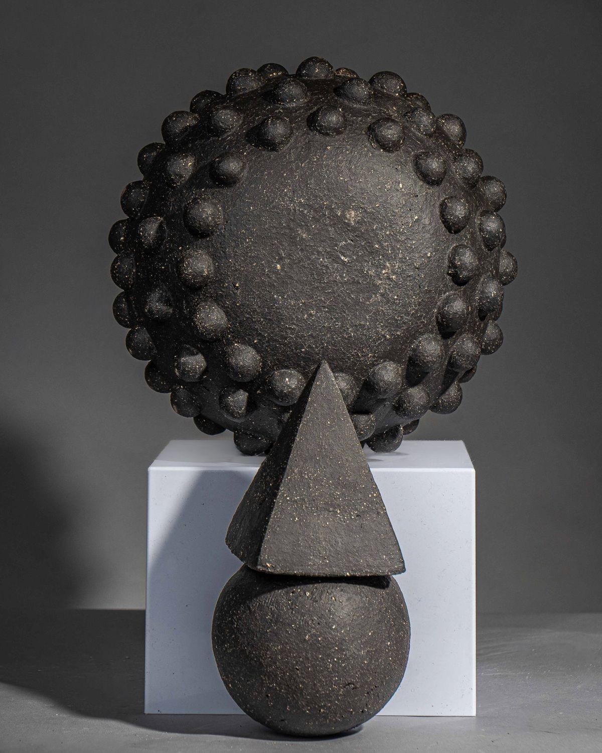Black textured studded sphere with a cone balanced on a sphere